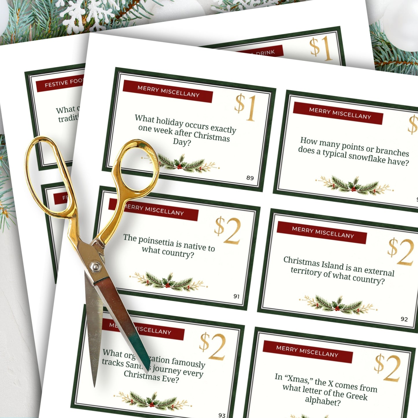 A set of Christmas-themed miscellany trivia cards arranged in a fan shape, with gold-handled scissors resting on top. The cards feature festive red headers, gold and black text, and holiday green borders with pine and holly illustrations.