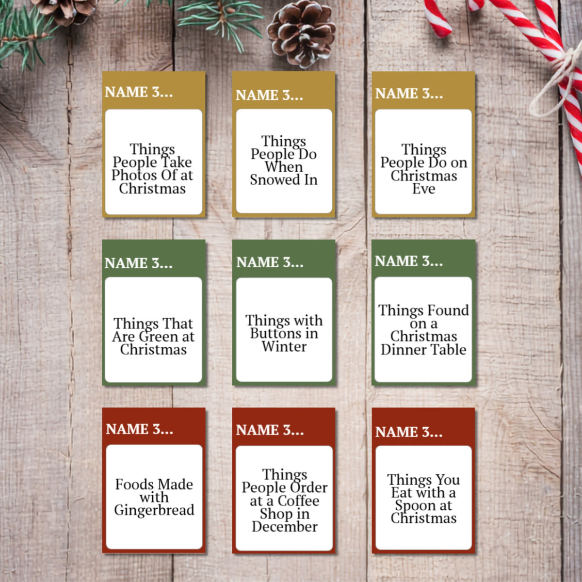 Nine Christmas-themed name cards arranged in a 3x3 grid on a rustic wooden background, decorated with pine branches, a pinecone, and a candy cane. Each card has a different holiday color header (gold, green, or red) and a white text box with customizable prompts like 'Things People Take Photos Of at Christmas' and 'Foods Made with Gingerbread'.